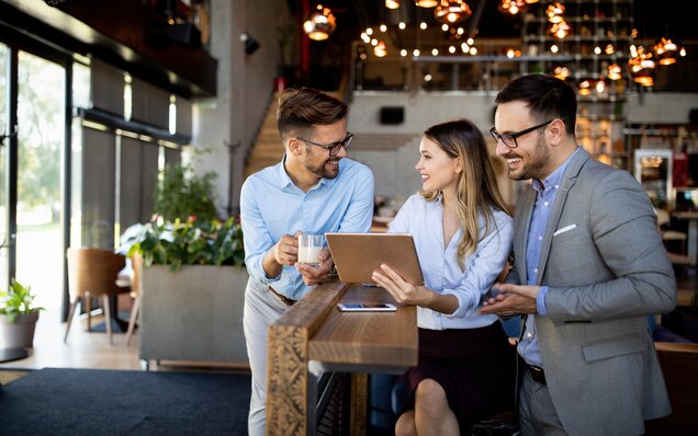 Trois professionnels discutent avec une tablette dans un café moderne