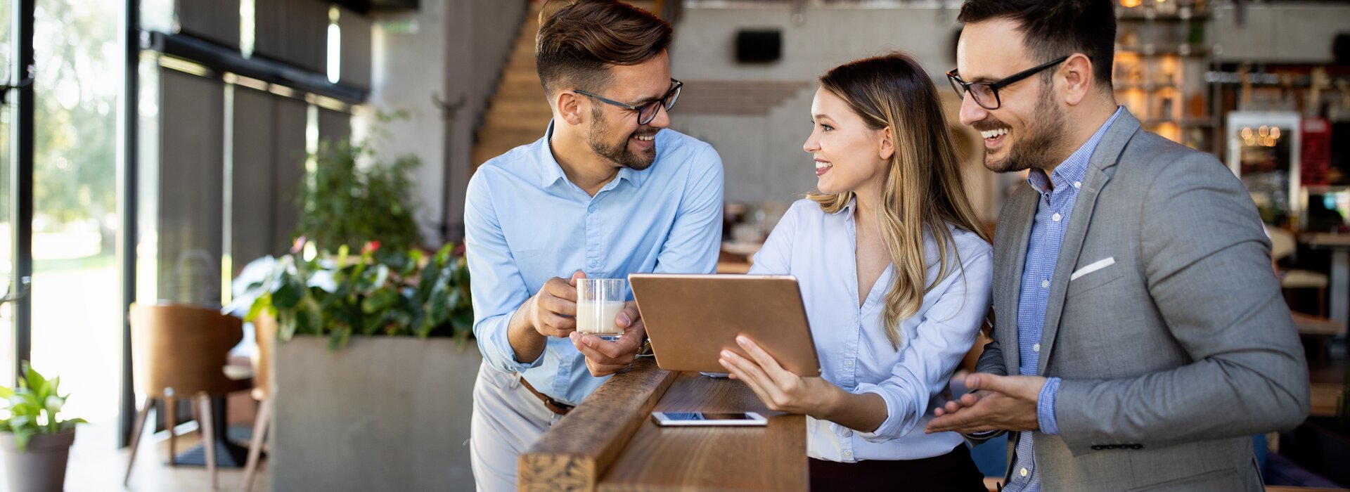 Trois professionnels discutent avec une tablette dans un café moderne
