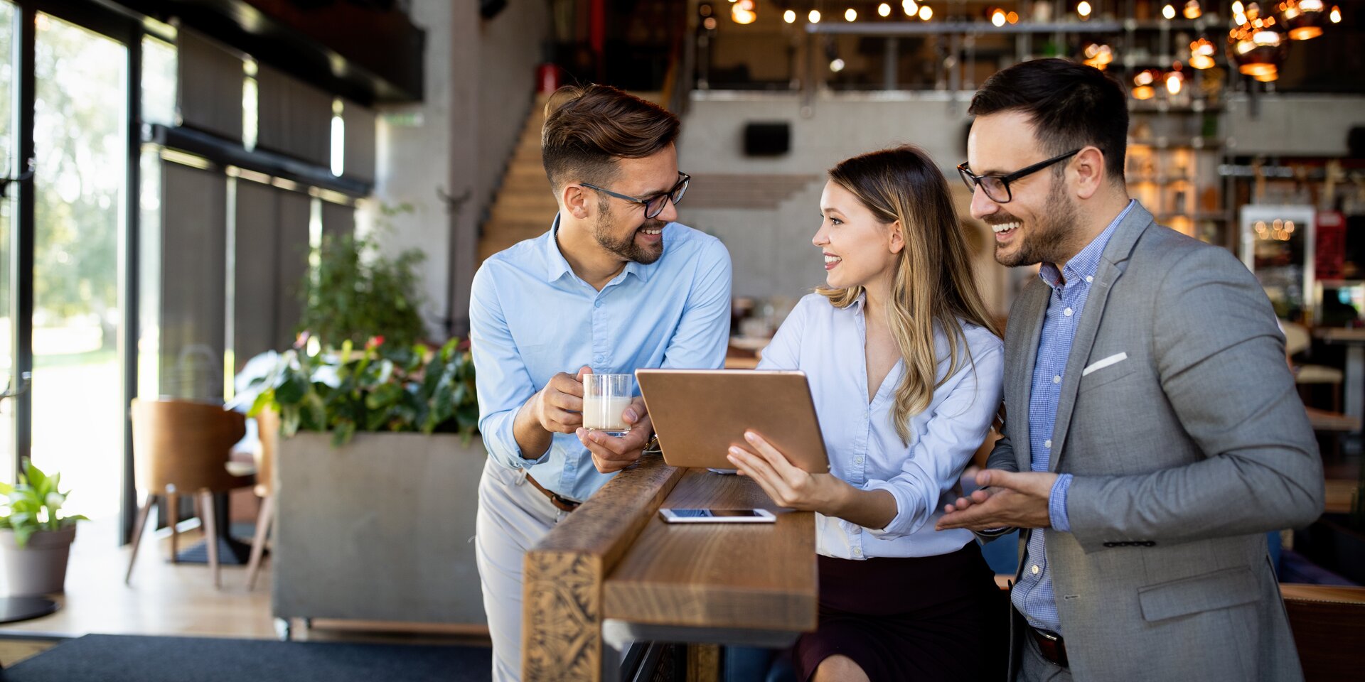Trois professionnels discutent avec une tablette dans un café moderne
