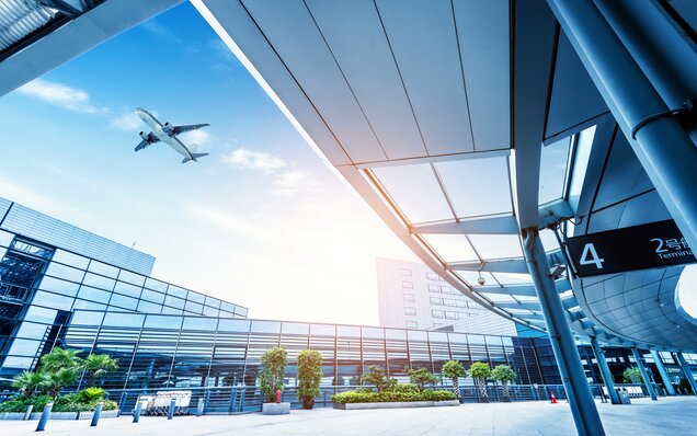 Avion en approche au-dessus d’un terminal d’aéroport moderne avec de grandes façades vitrées